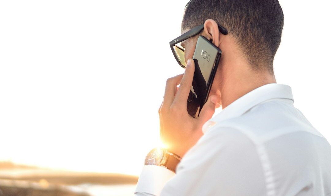 Man holding smartphone standing in front of calm body of water