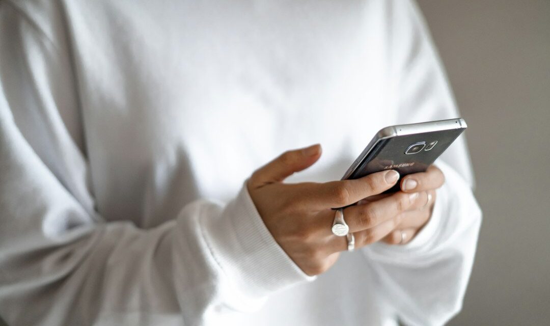 Person in white long sleeve shirt holding black smartphone