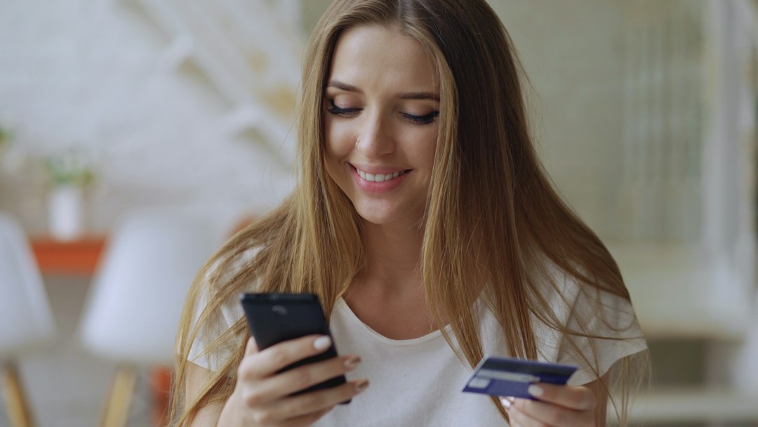 Young woman smiling while holding phone and credit card