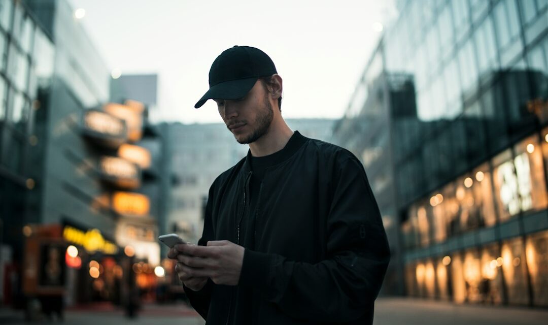 Man in black jacket wearing black fitted cap while using phone