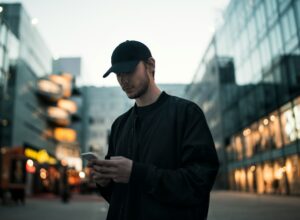Man in black jacket wearing black fitted cap while using phone