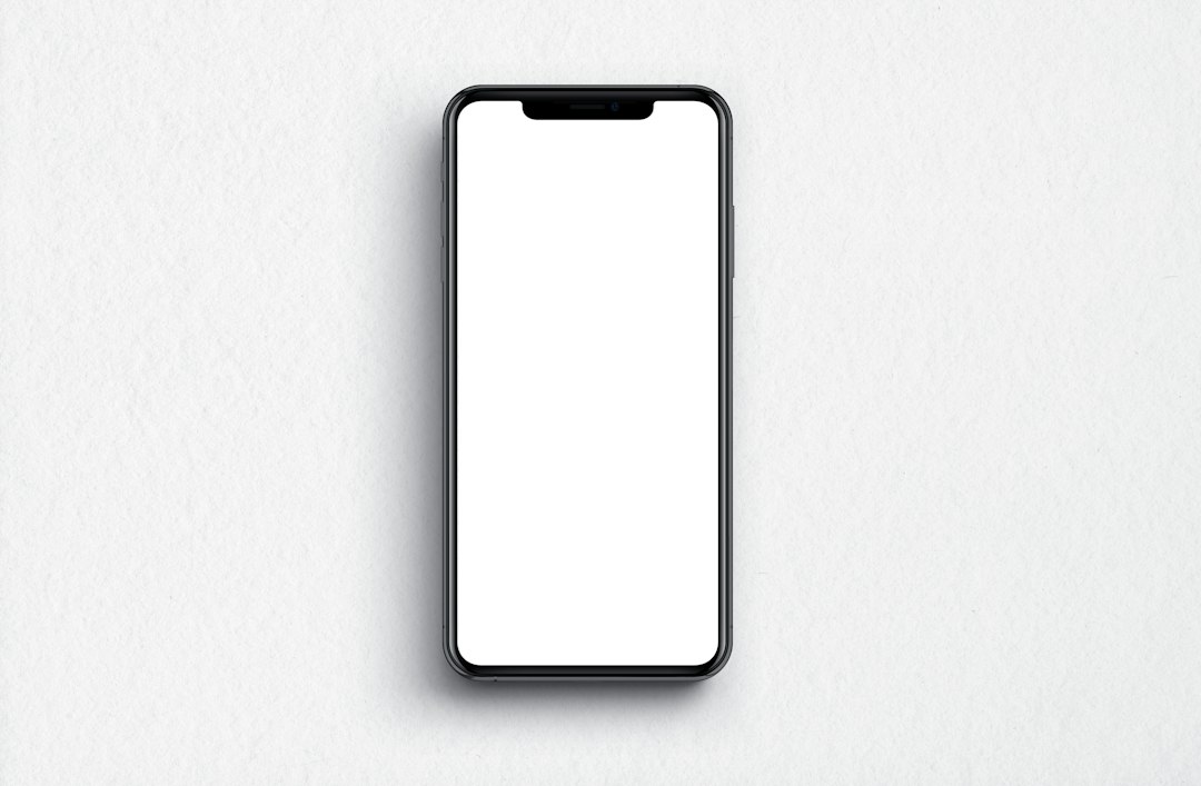 A black smartphone with a blank white screen on a textured white surface