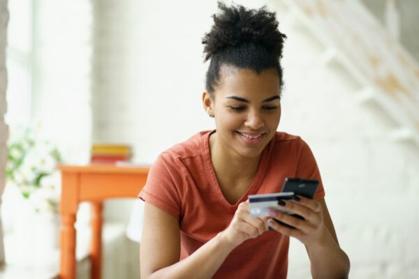 Young woman smiling while holding credit card and phone