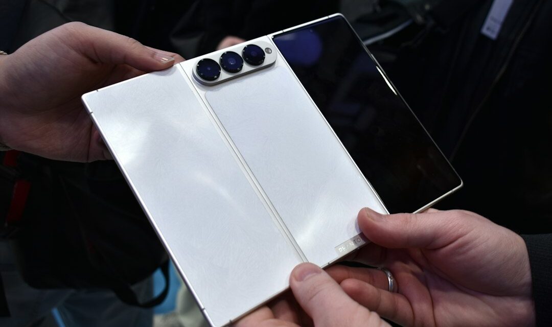 Hands hold a white foldable smartphone with three cameras