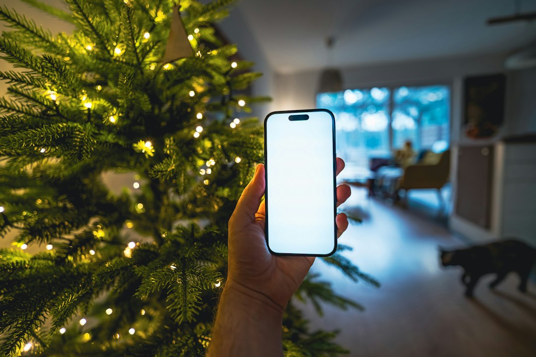 Hand holding smartphone in front of christmas tree