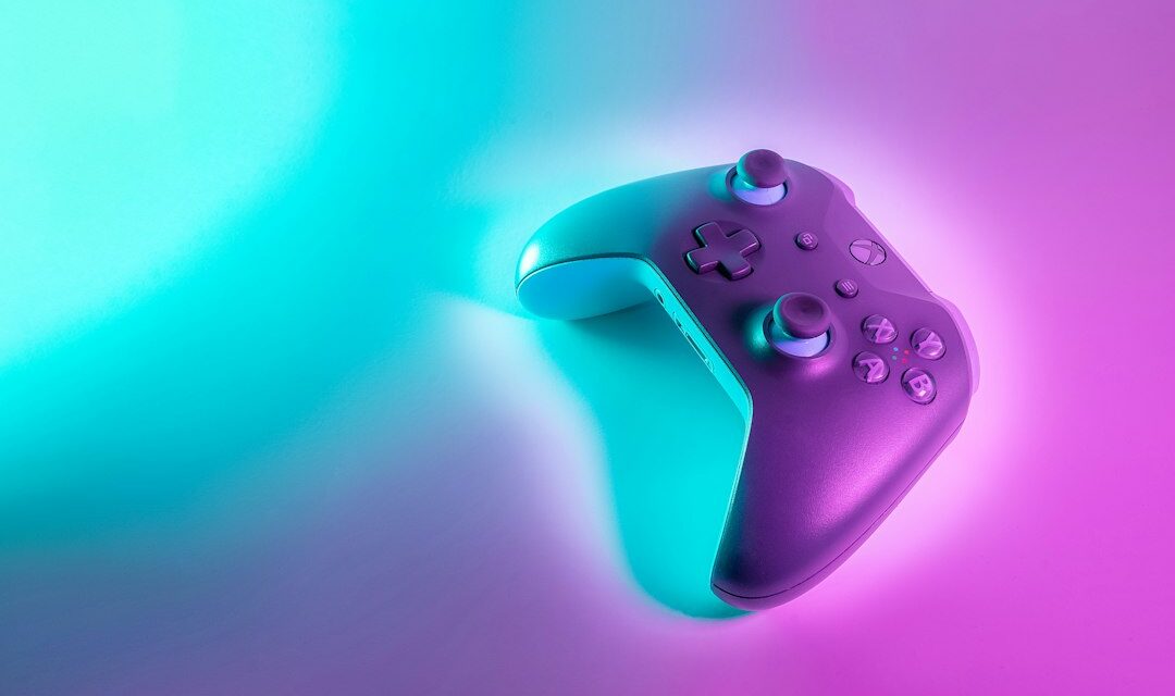 A wireless game controller illuminated by vibrant cyan and magenta neon light