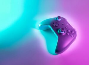 A wireless game controller illuminated by vibrant cyan and magenta neon light