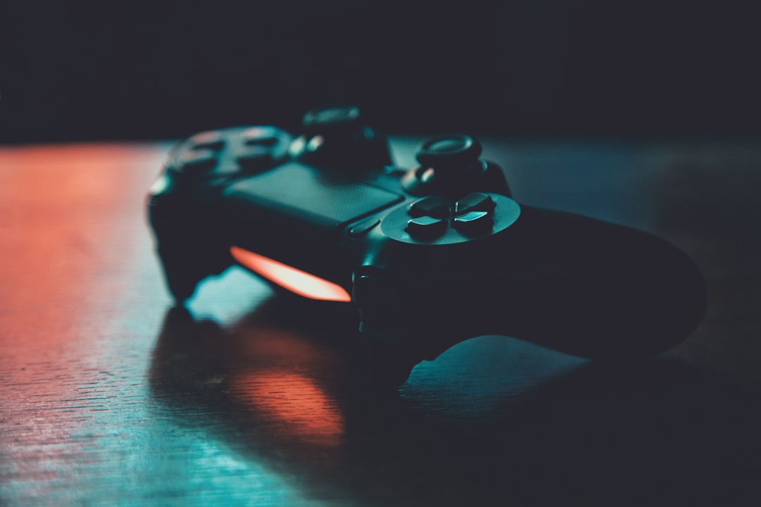 A black game controller on a wooden surface with blue and orange lighting