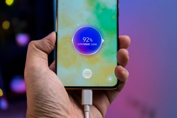 A person holding a cell phone with a charger in their hand