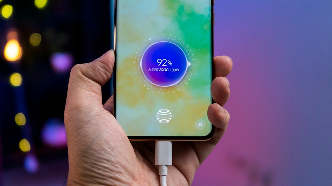 A person holding a cell phone with a charger in their hand