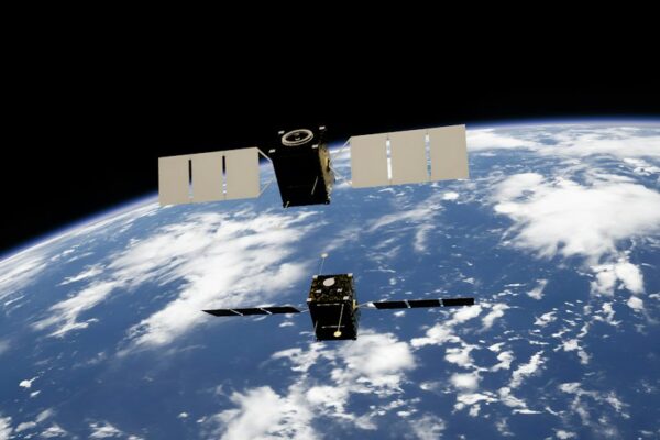 Two satellites with solar panels orbiting above the blue Earth with white clouds