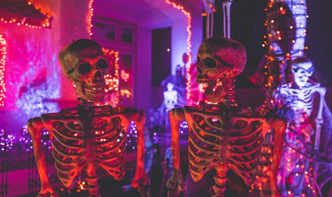 Two skeleton near white concrete building with string lights at daytime